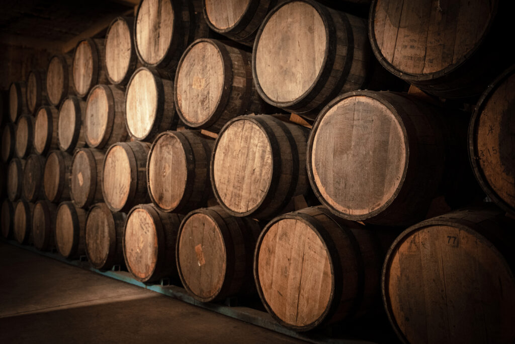 Rows of oak barrels stacked in a dimly lit tequila aging cellar, receding into the distance.