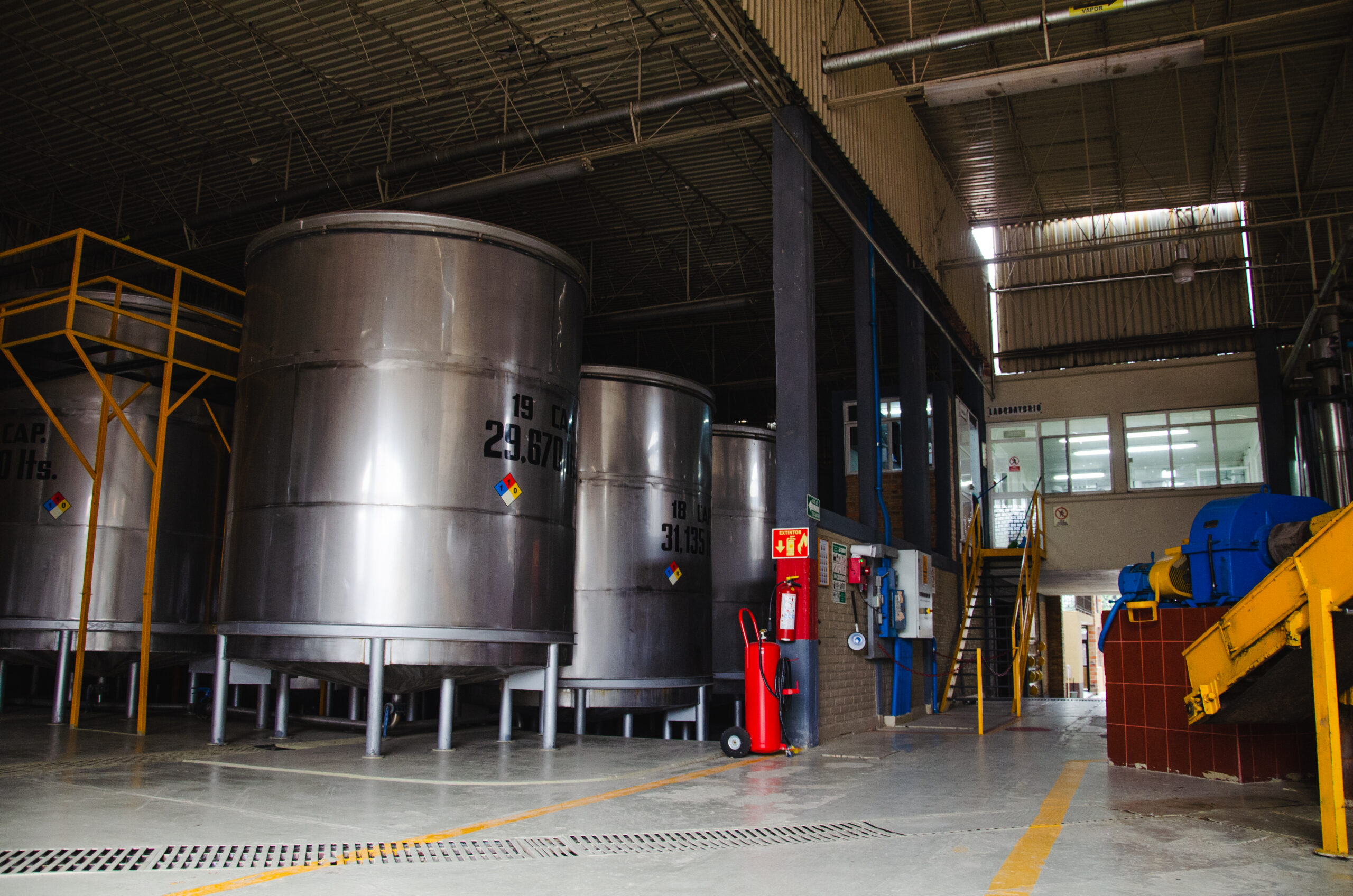 Large stainless steel fermentation tanks inside a tequila distillery production facility, where agave is fermented before the distillation process.