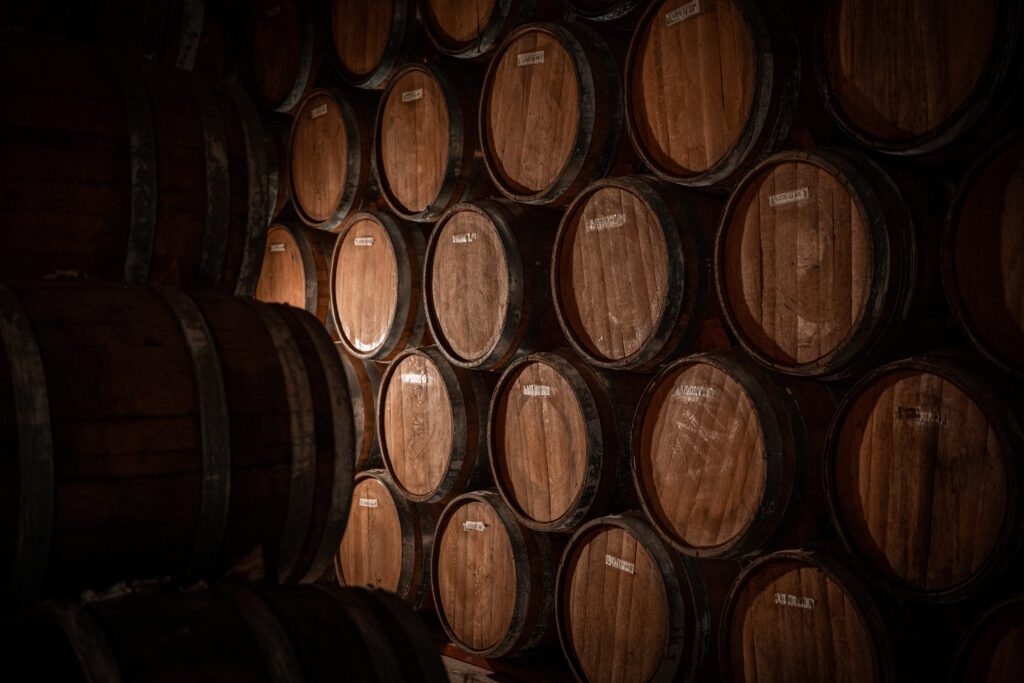 Stacked oak barrel ends in a dimly lit tequila aging cellar, each labeled "Lote 53 AR."
