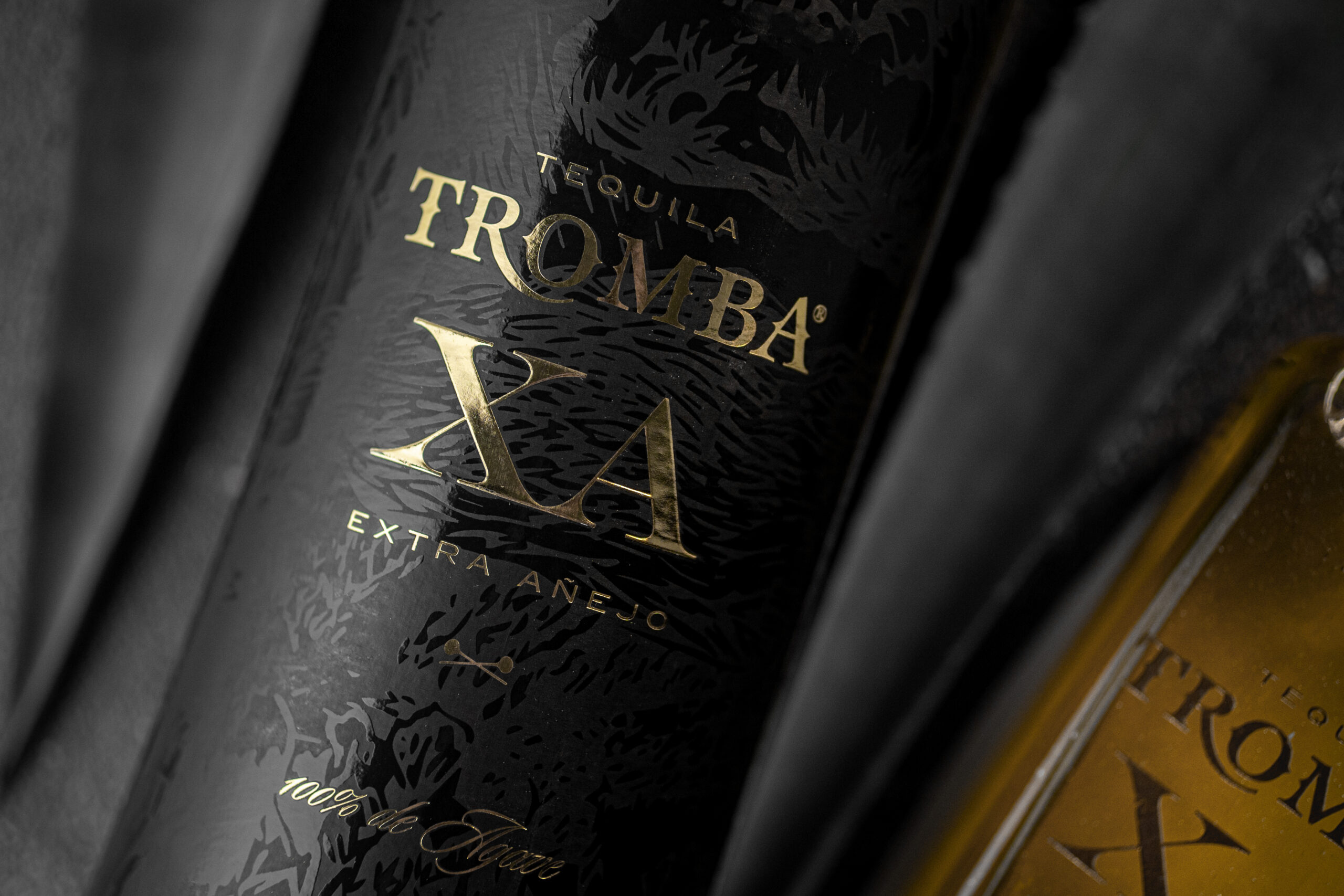 Close-up of a black Tromba Tequila XA Extra Añejo bottle with gold lettering and agave-leaf embossing.